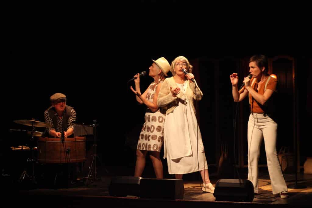 Tri o féminin Y Akapella sur scène avec un percussionniste.